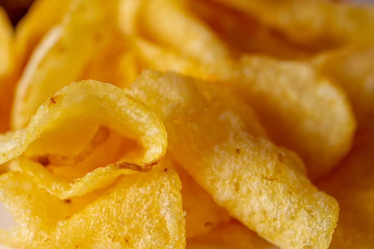 Warm golden kettle chips filling the frame, folds and bubbles sharp in the light