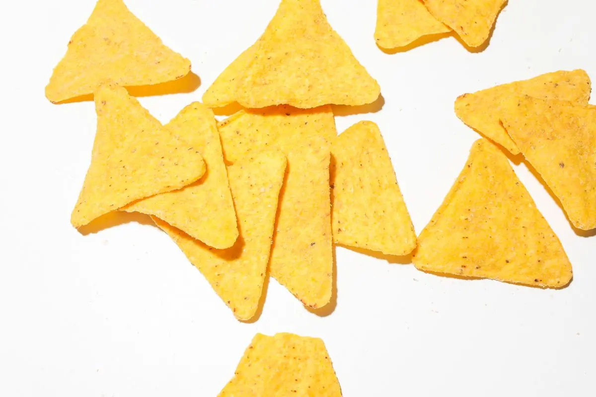 Golden tortilla-cut chips scattered on a bright white ground with hard shadows