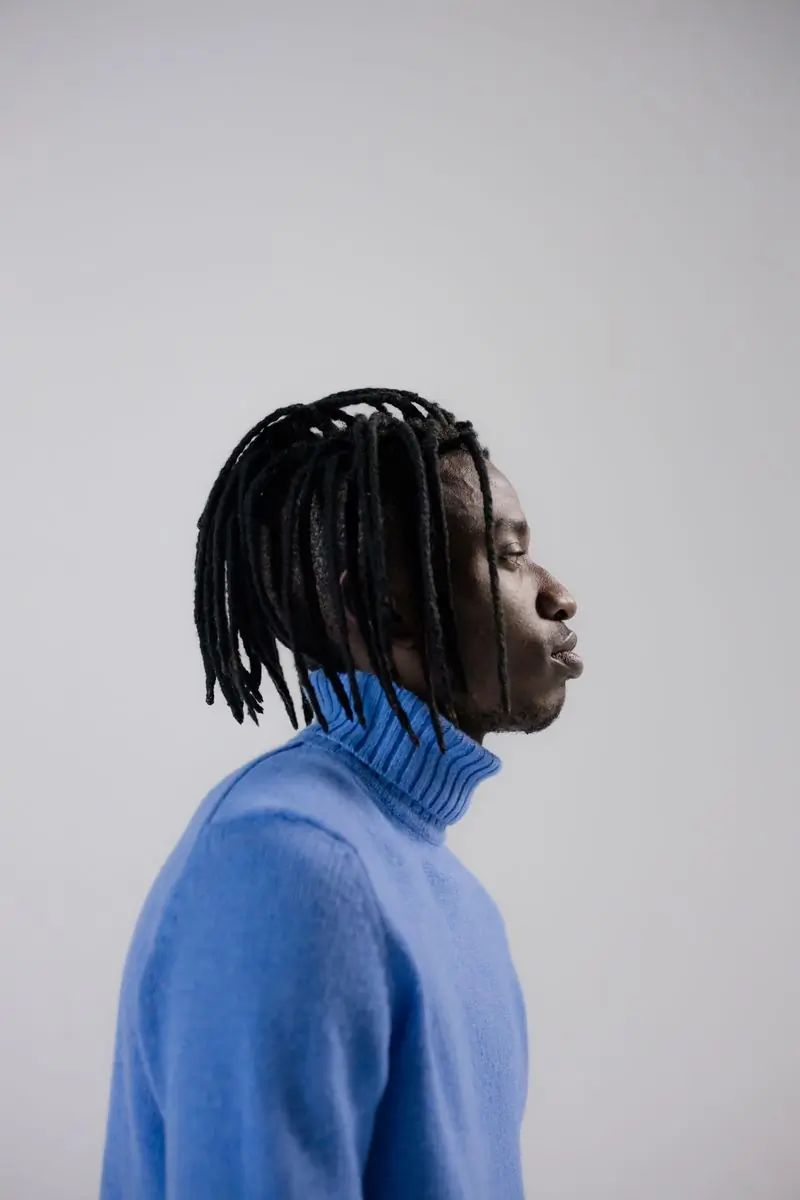 A man with locs in a blue turtleneck photographed in profile