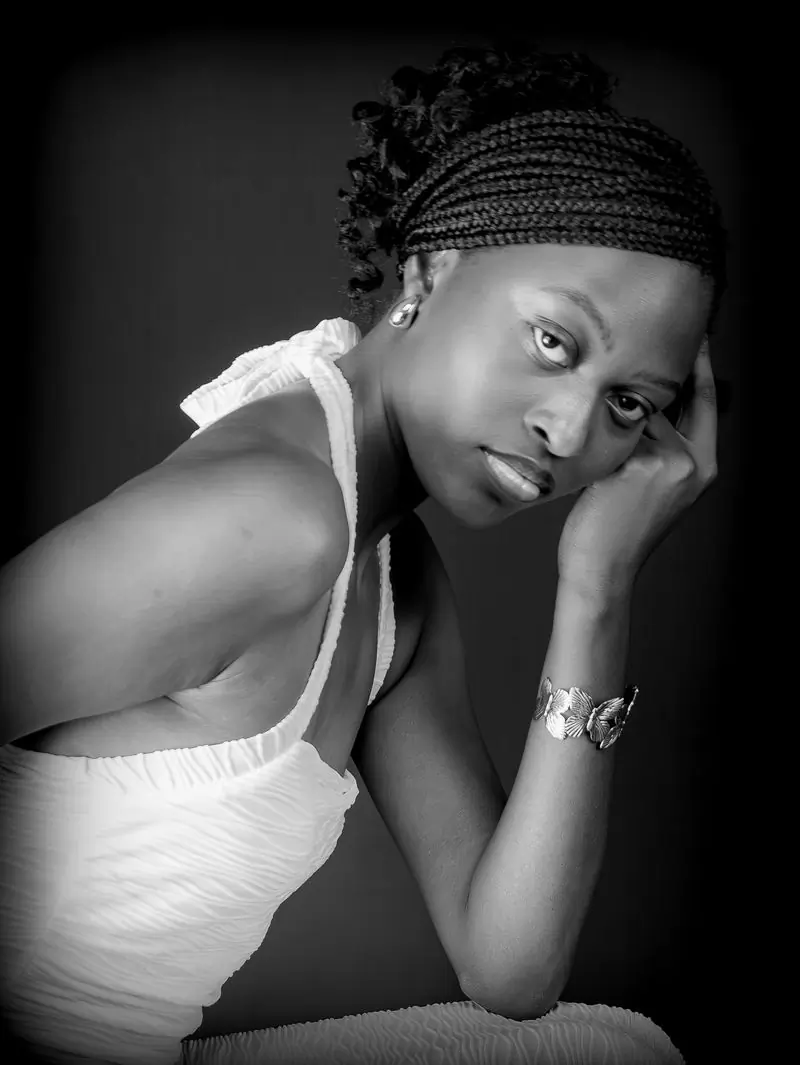 A woman with braids resting her head on her hand, photographed in black and white