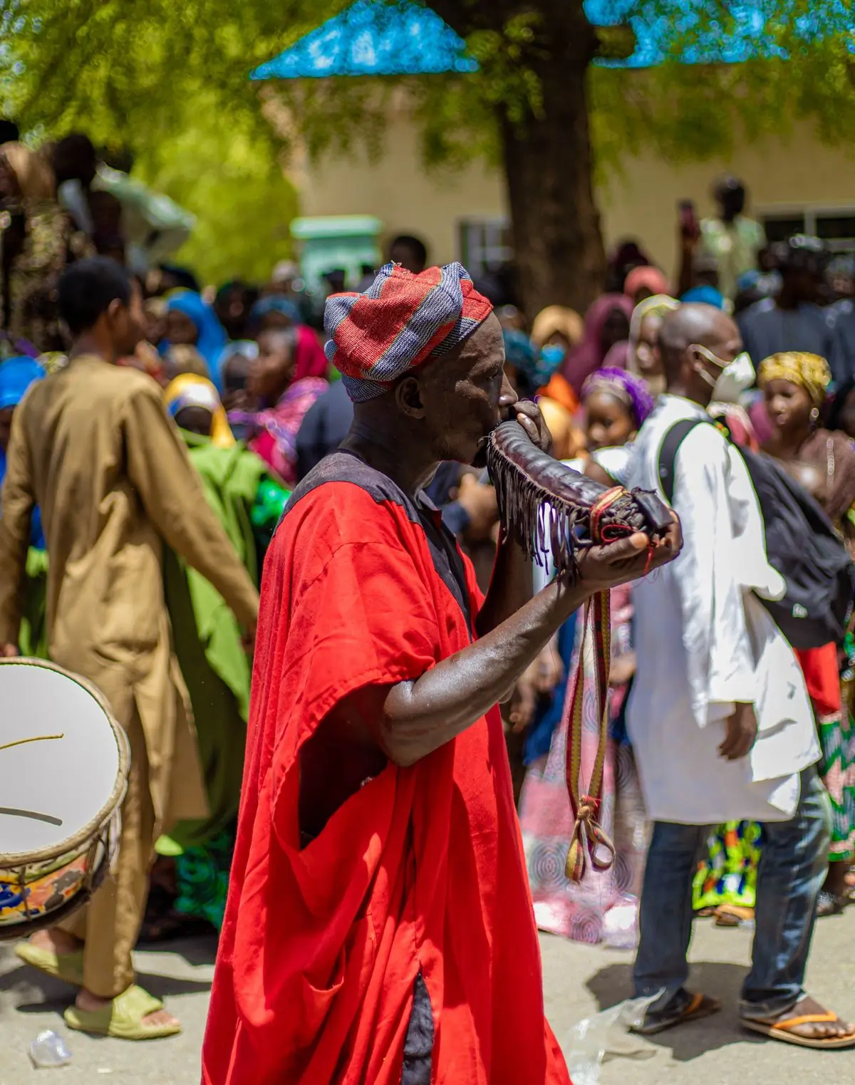 A man in a red robe blowing a carved horn in a crowded procession