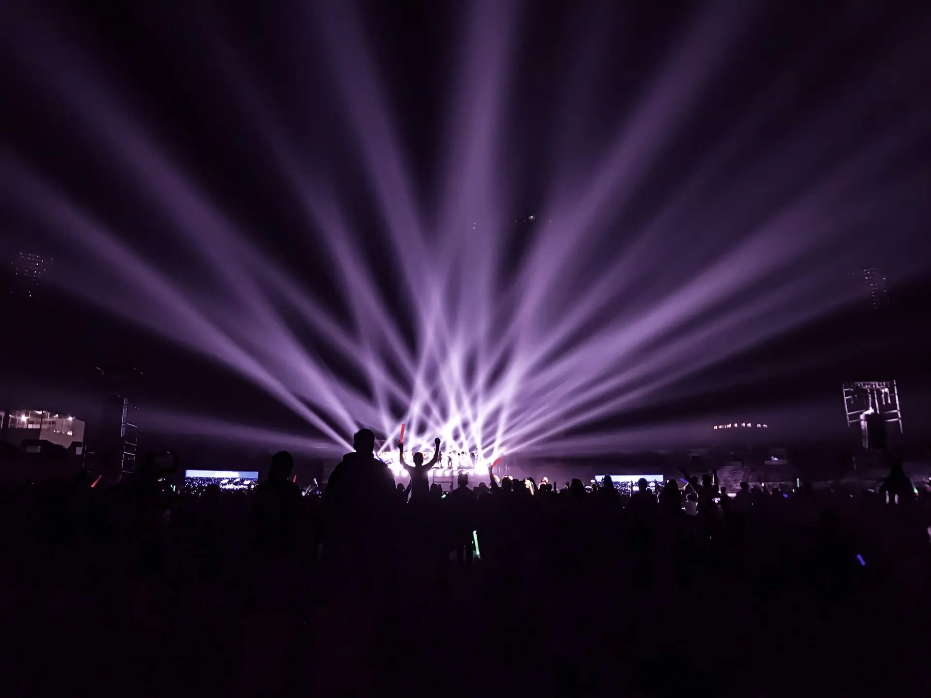 A fan of purple beams over the heads of a crowd at a night concert