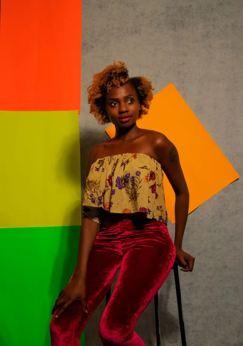 A performer in printed cloth standing against blocks of orange and green