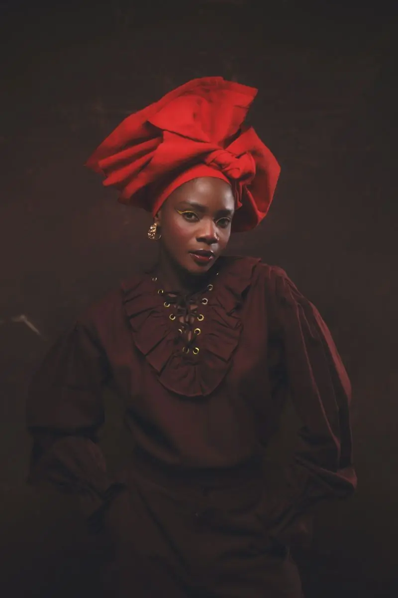 A vocalist in a red headwrap photographed against a dark ground