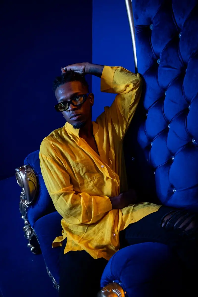 A producer in a yellow shirt seated against a blue backdrop