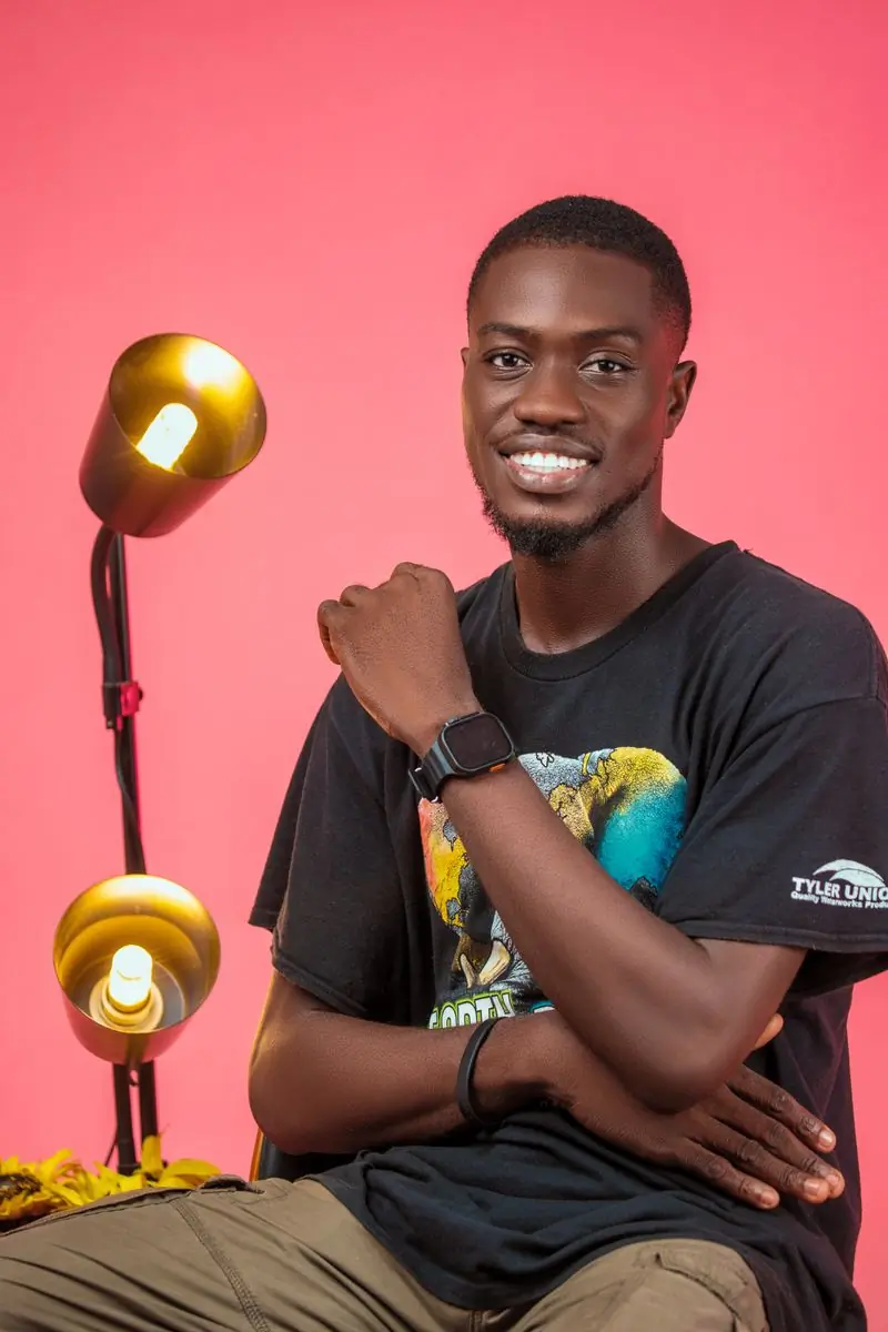 A smiling man in a printed T-shirt photographed against a pink ground
