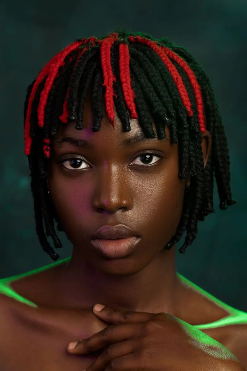 A woman with red and black braids looking straight to camera