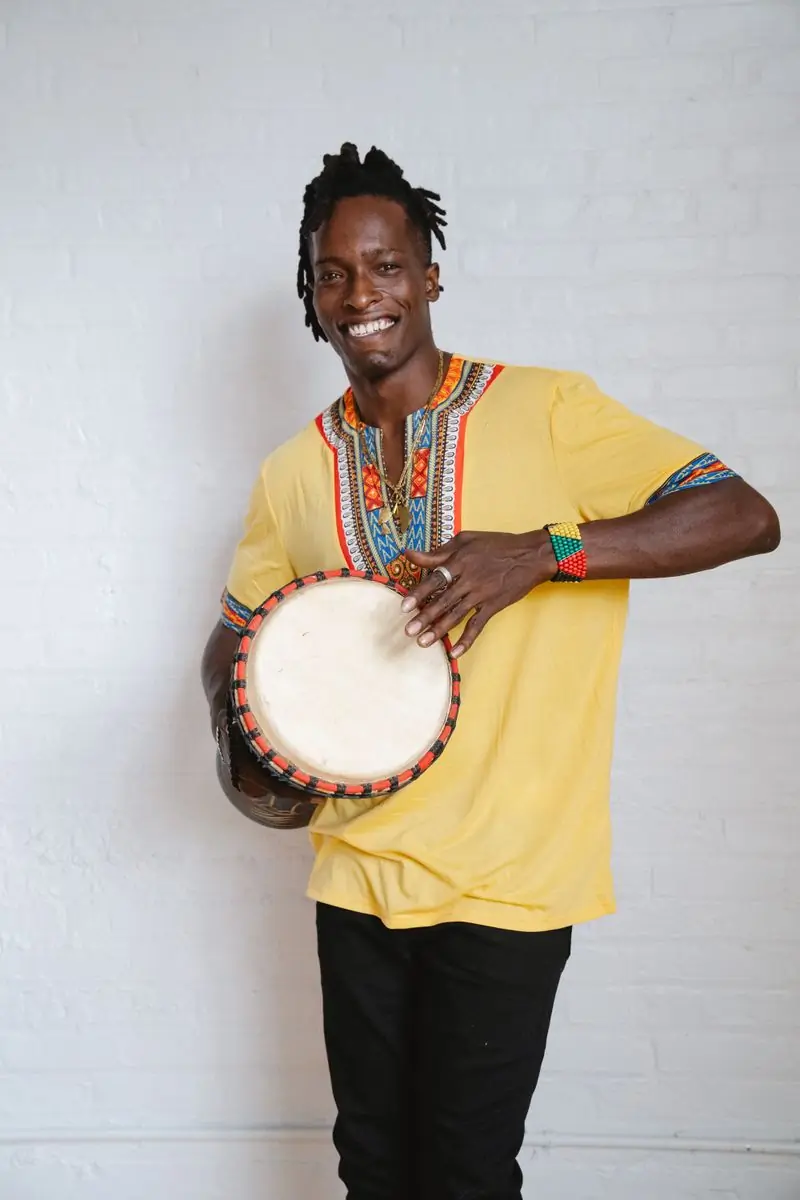 A drummer in a yellow smock holding a djembe