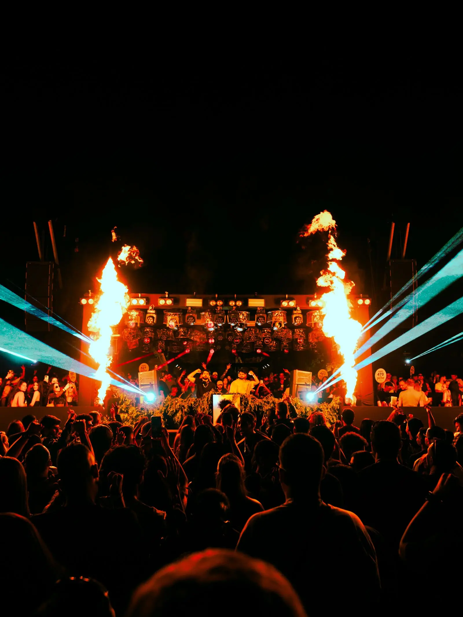 A night crowd in front of a lit stage with flame effects