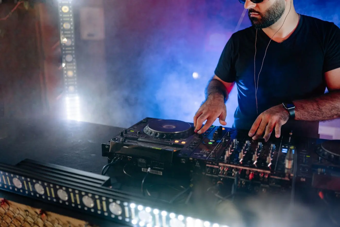 A DJ working a mixer under coloured light and haze