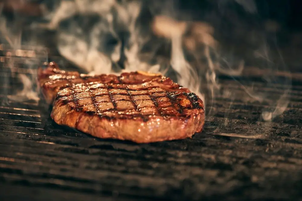 A steak roasting over an open grill with smoke rising