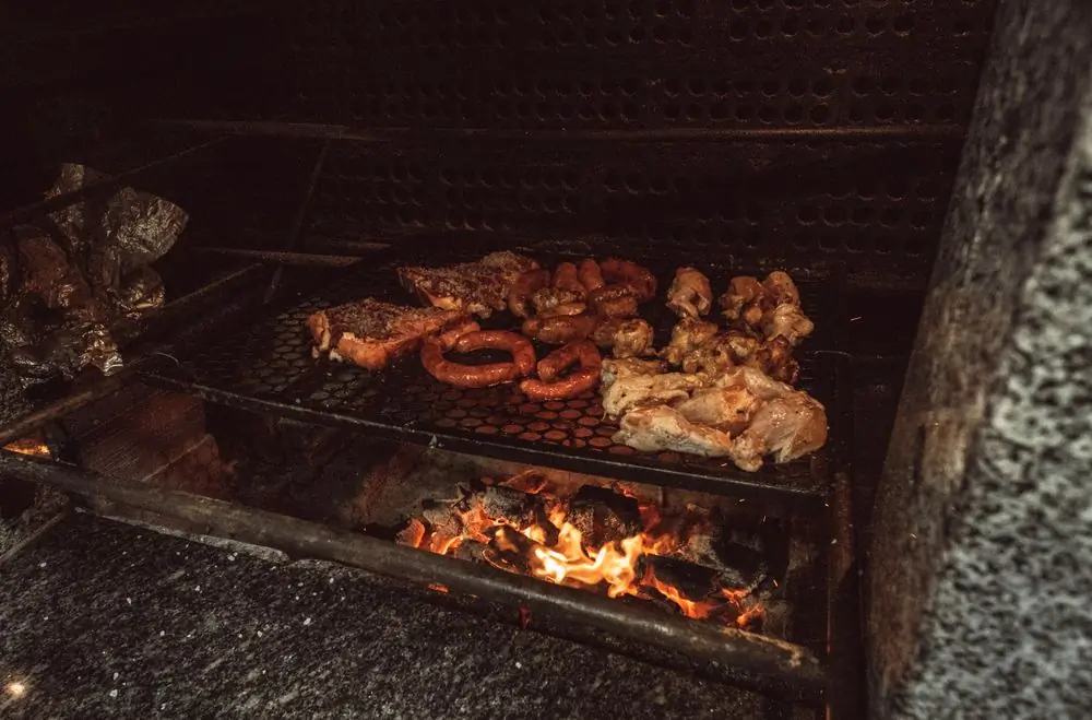 Assorted meats cooking over an open charcoal fire at night