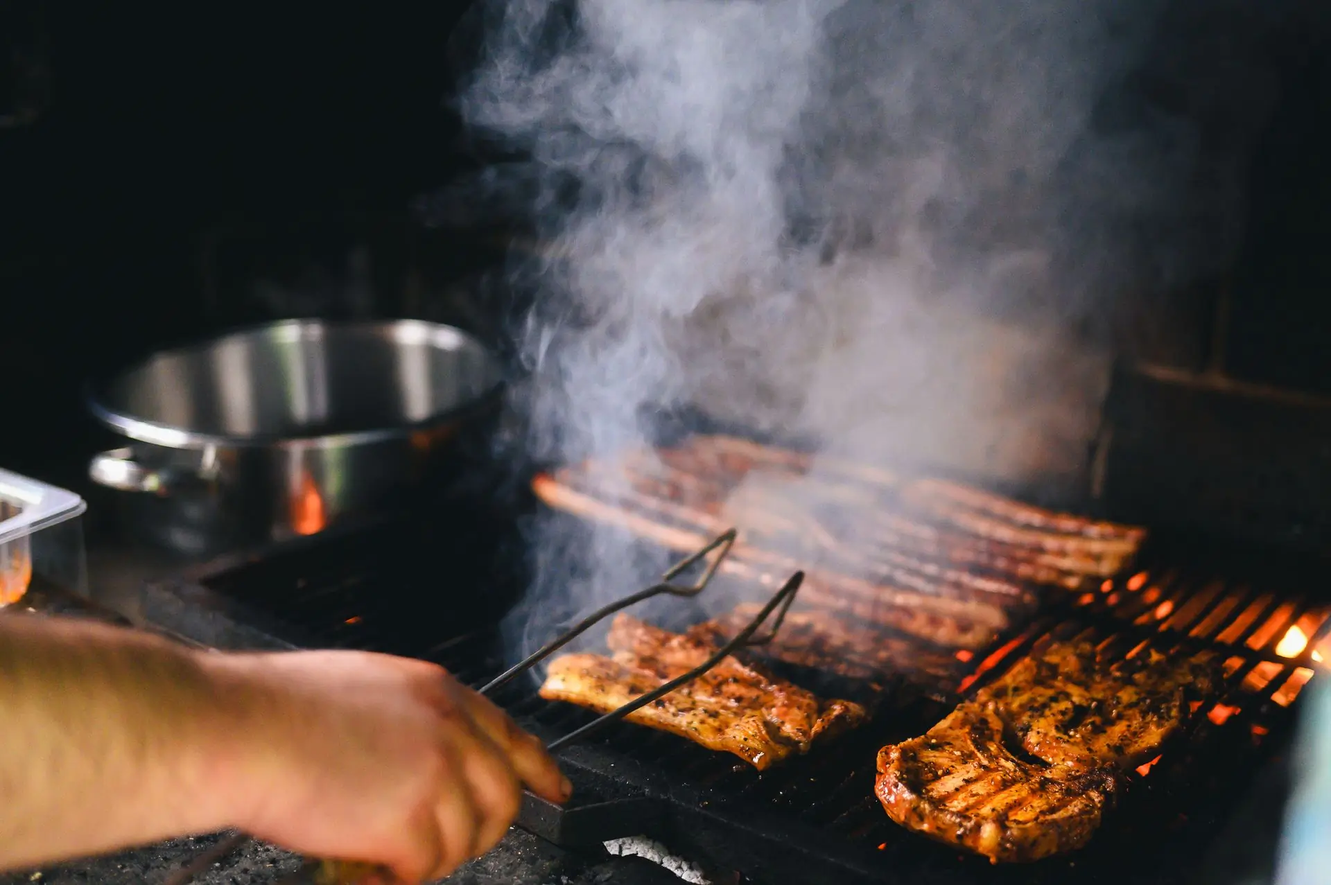 Meat grilling over the pit with smoke rising through the bars