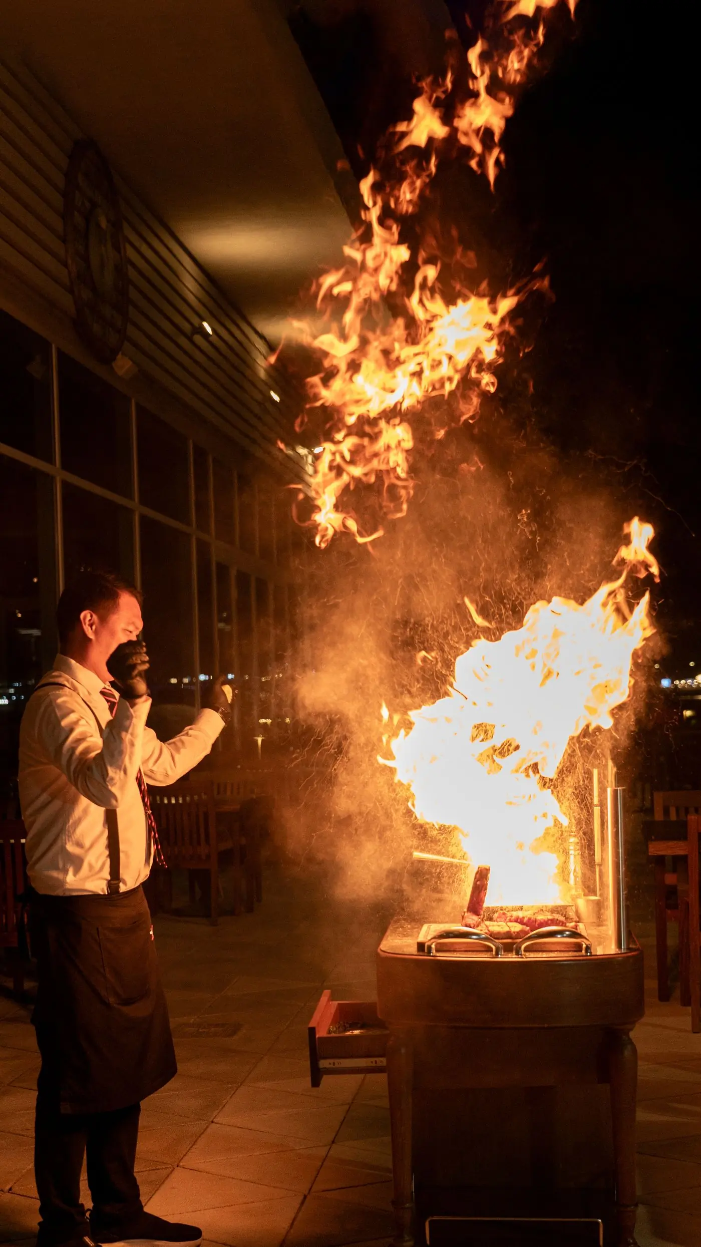 A cook working over a tall open flame in a dark kitchen