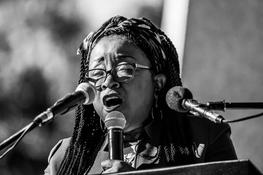 A vocalist at a microphone beside a keyboard, in black and white