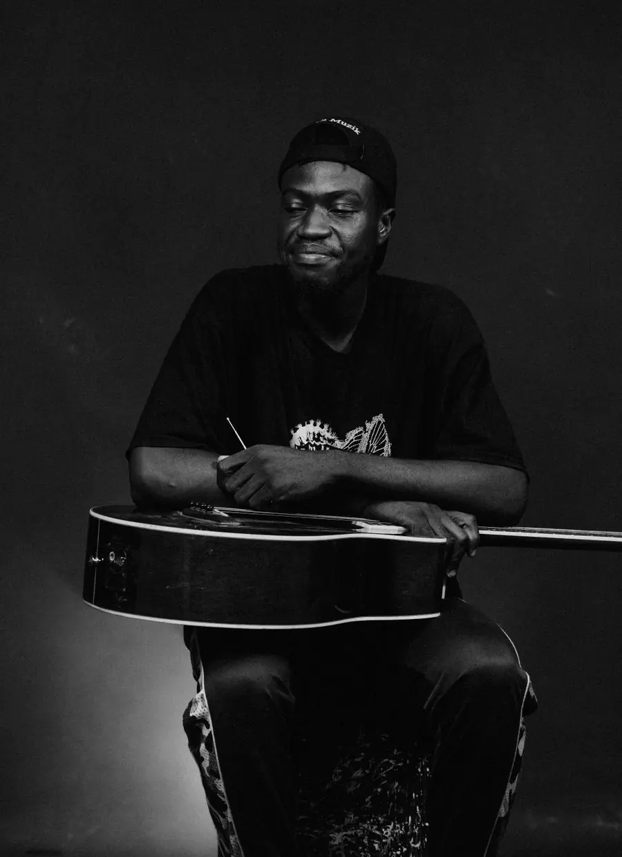 A guitarist holding an acoustic guitar, photographed in black and white