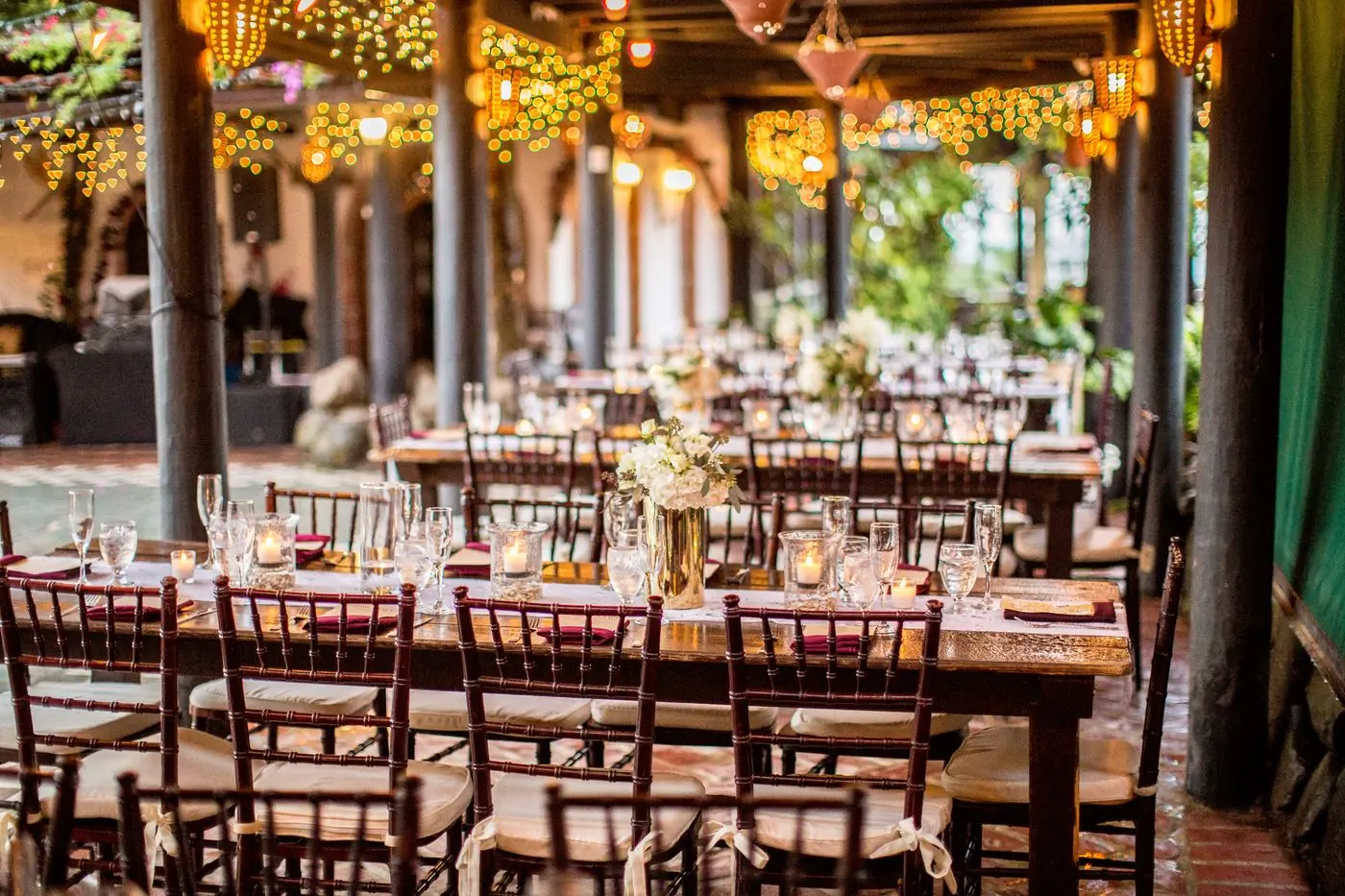 An outdoor dinner laid under warm bistro lights with floral centrepieces