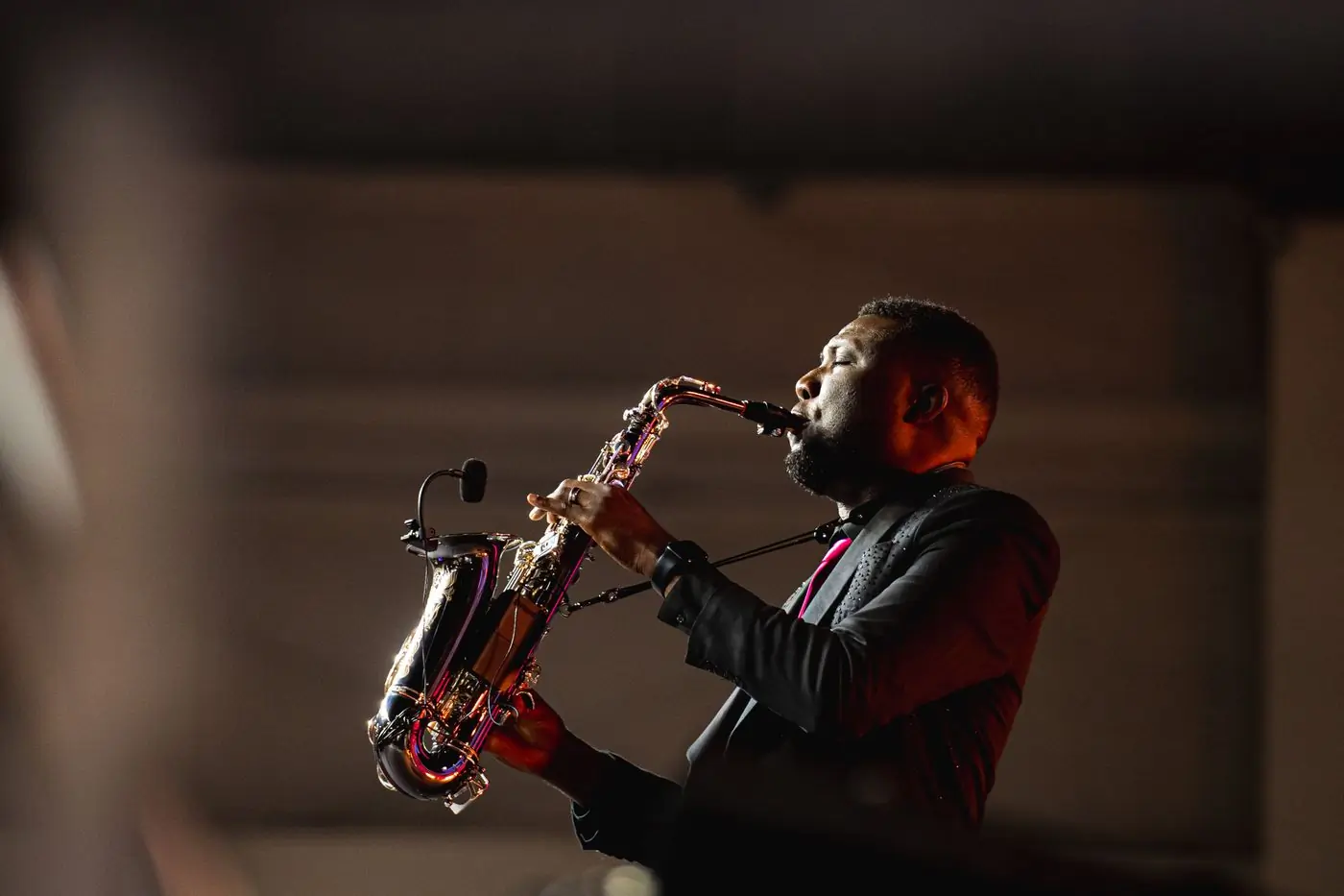 A saxophonist performing on stage under warm red light