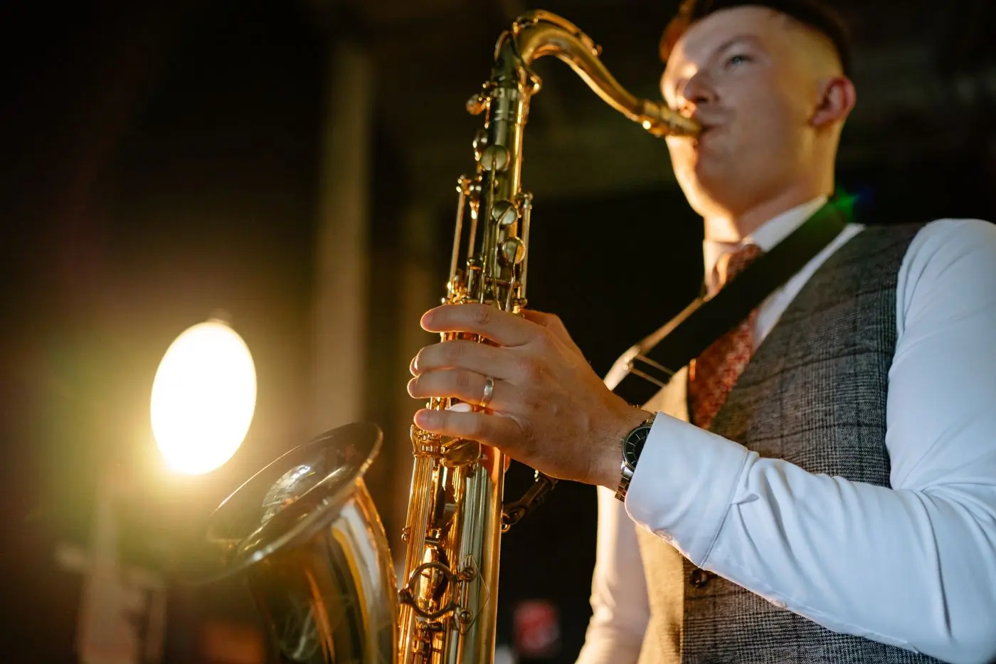 A saxophonist in a waistcoat playing under warm stage light