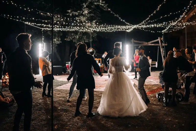 A bride dancing with guests under strings of fairy lights