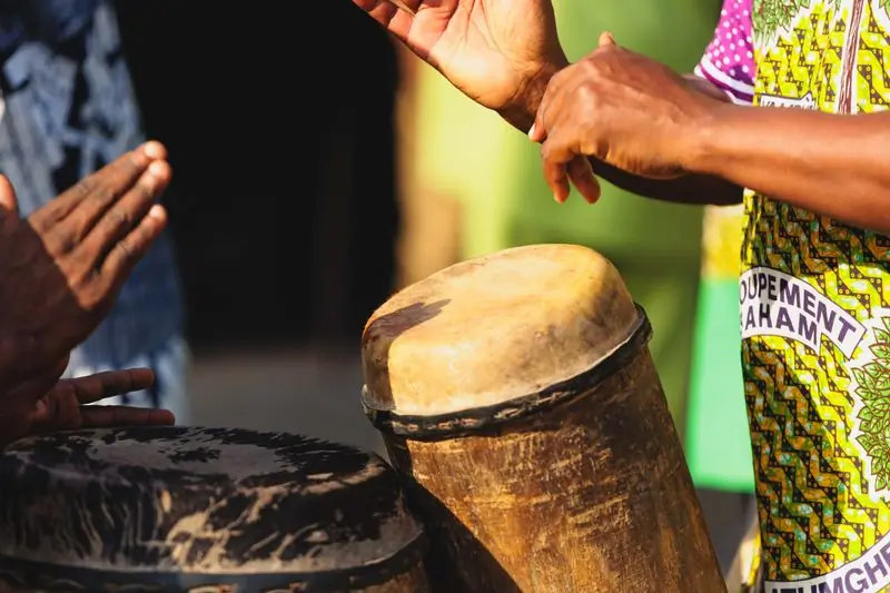 Hands playing a traditional drum in kente cloth