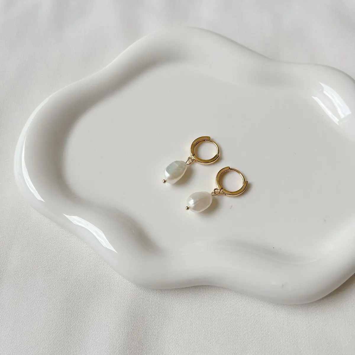 A gold chain and two rings resting in a small ceramic dish on a linen cloth