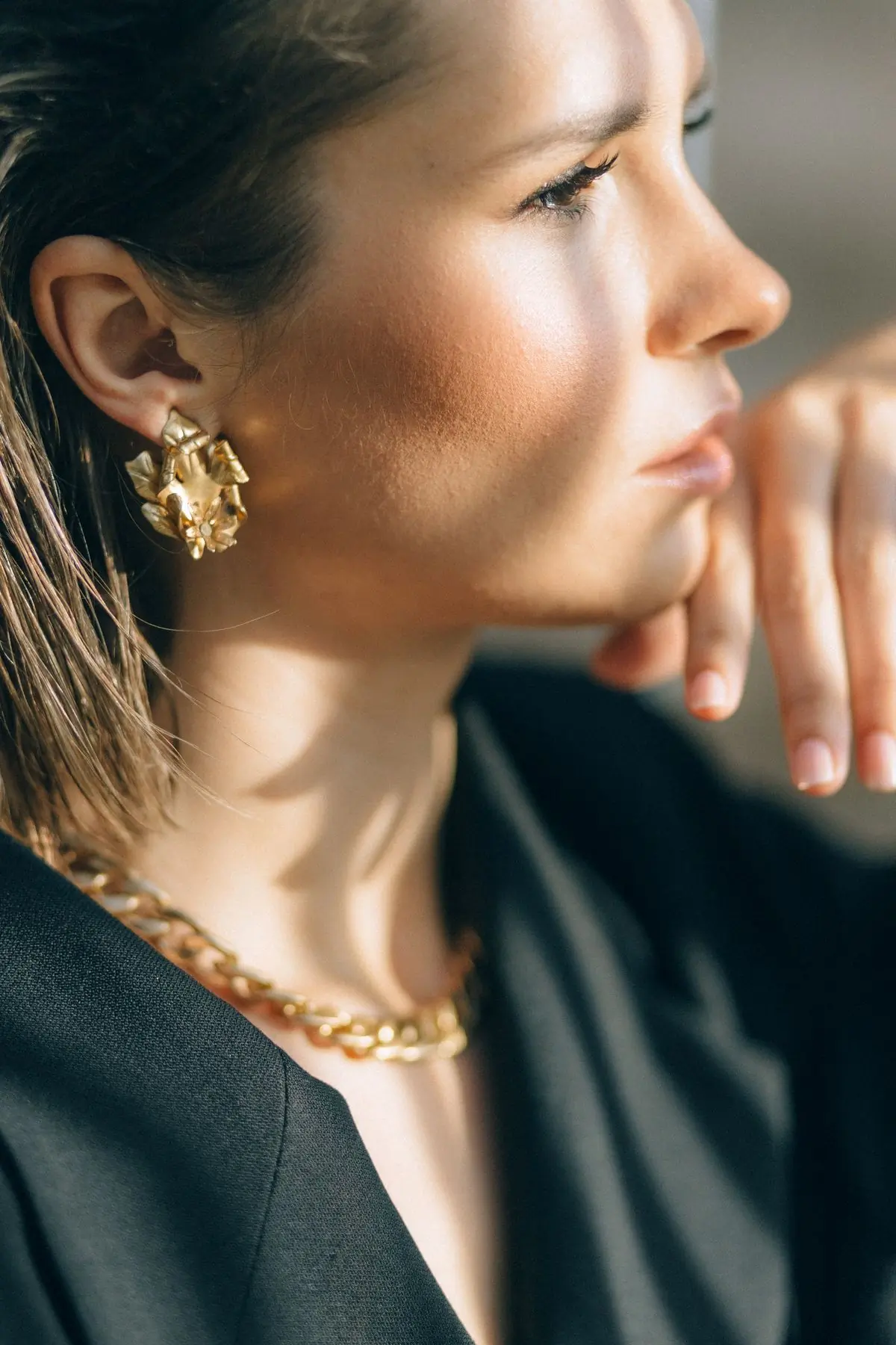 Sunlit profile of a woman wearing a sculptural gold leaf earring and a chain necklace