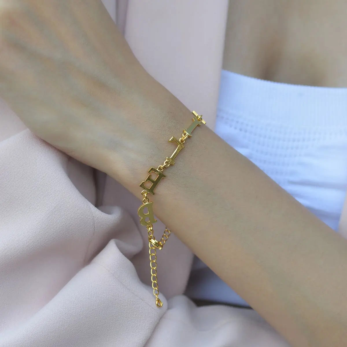 A wrist wearing a gold chain bracelet and a cast bangle