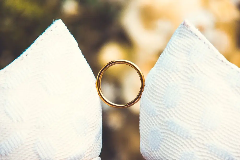 The plain gold band of the pair, held between folds of white fabric in warm light