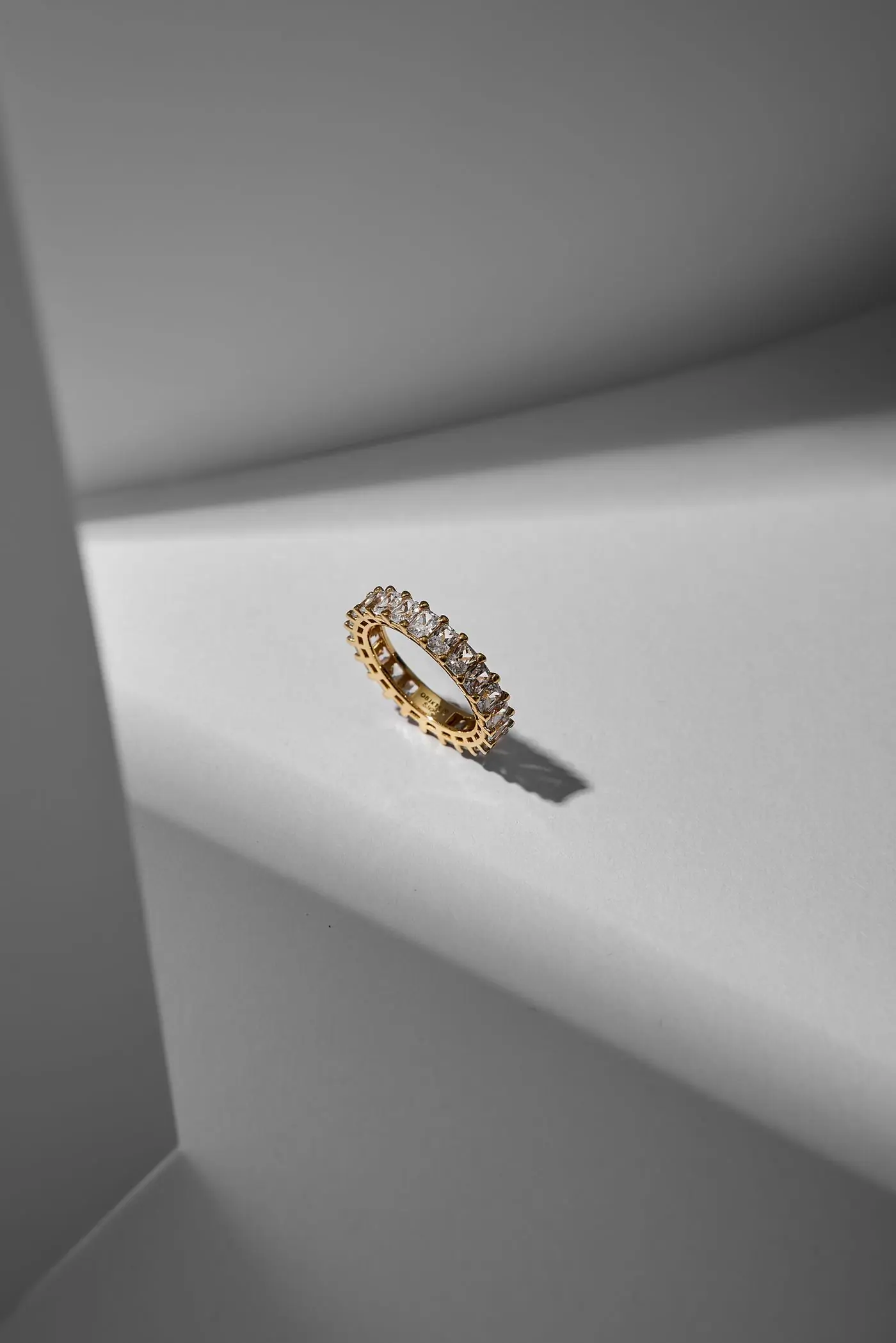 The Ama Solitaire's diamond-set band seen in macro, casting a long soft shadow on a pale ledge