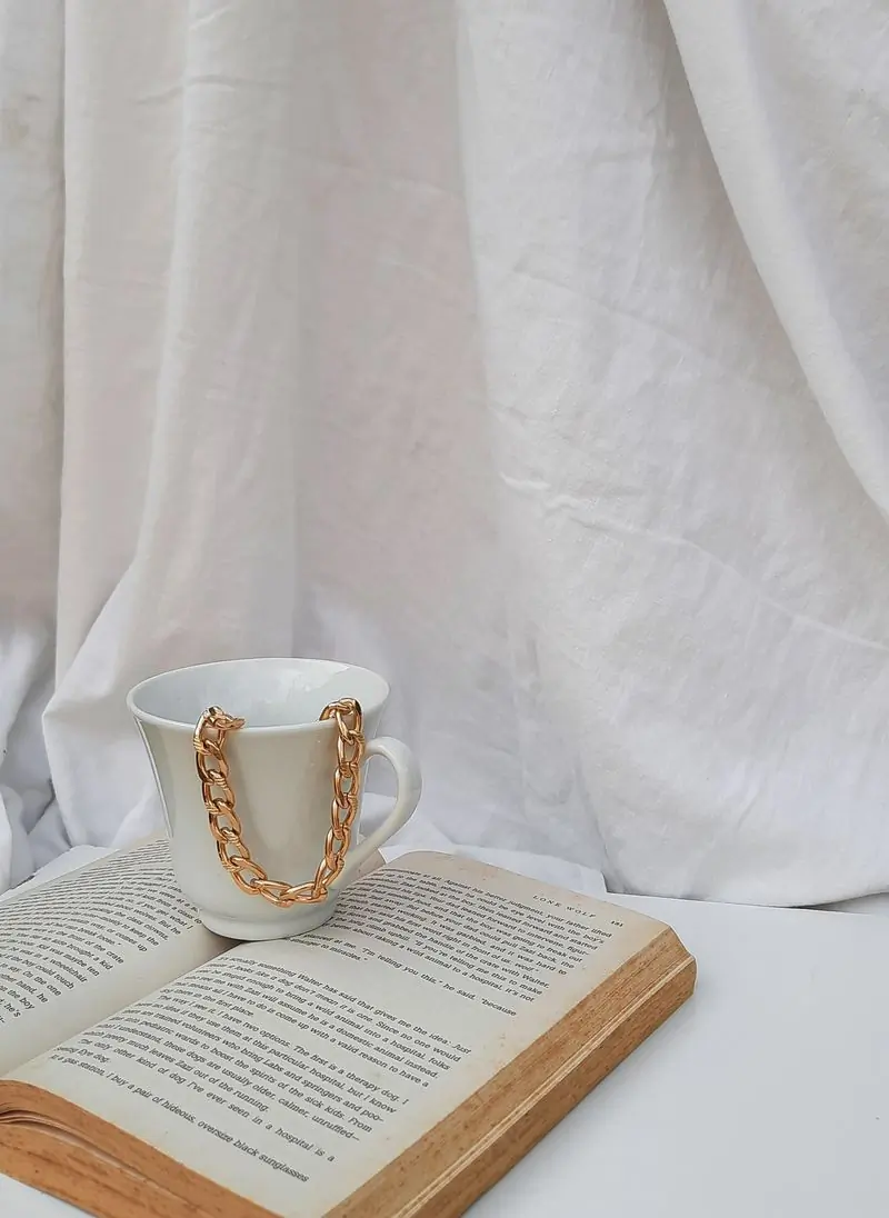 A gold chain spilling from a white ceramic mug set on an open book