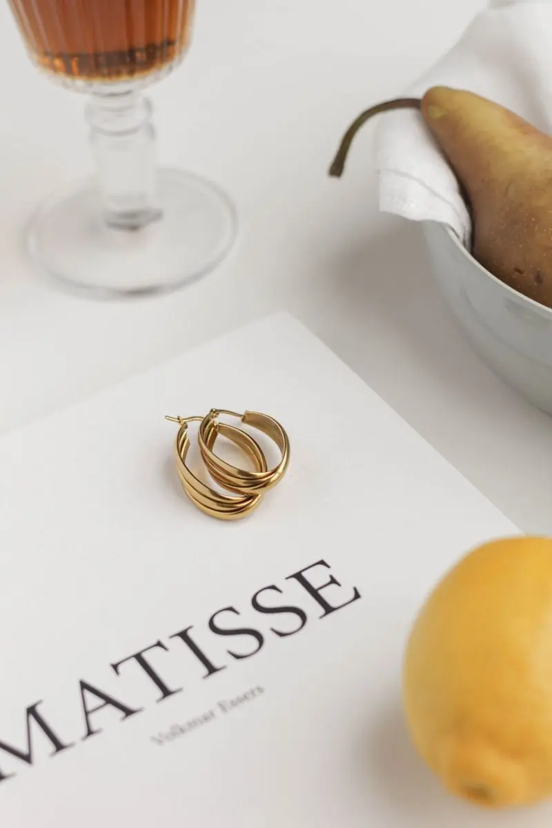 Twisted gold hoop earrings resting on an art book beside a lemon on a white table
