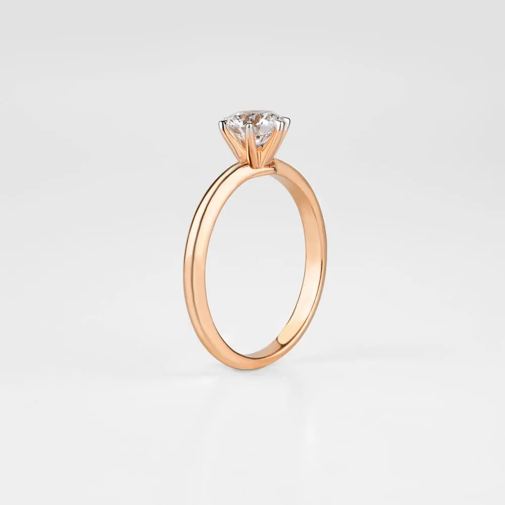 A gold solitaire engagement ring on a pale ground