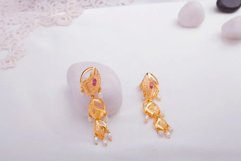 A pair of gold and pearl drop earrings on a white ground