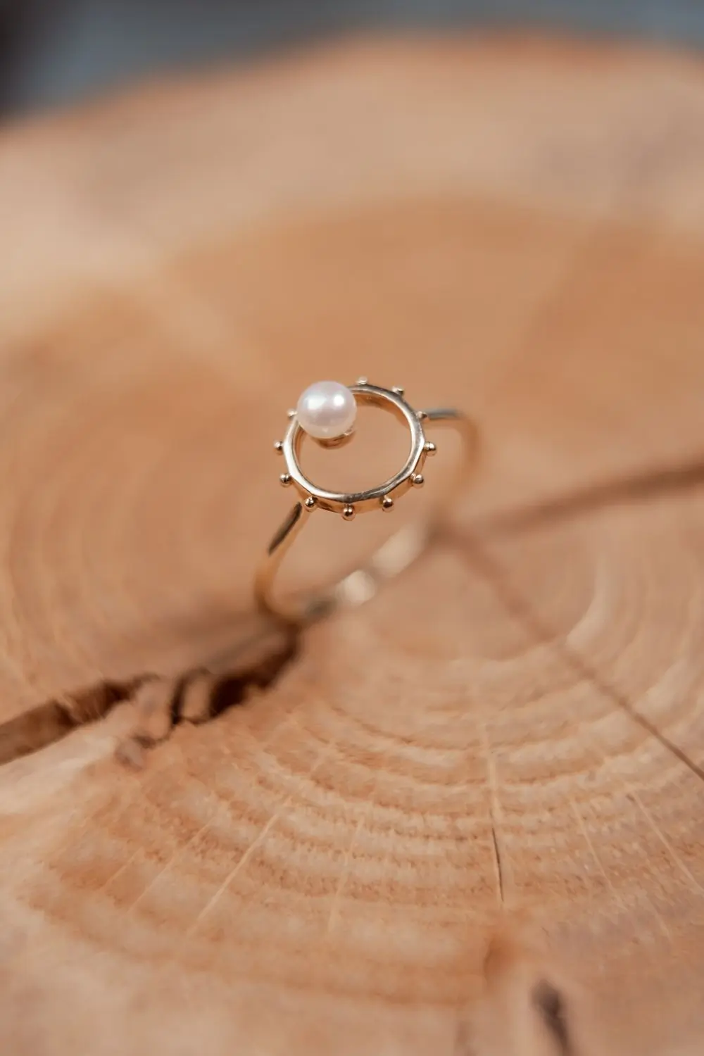 A gold ring holding a single round pearl, photographed on a white ground