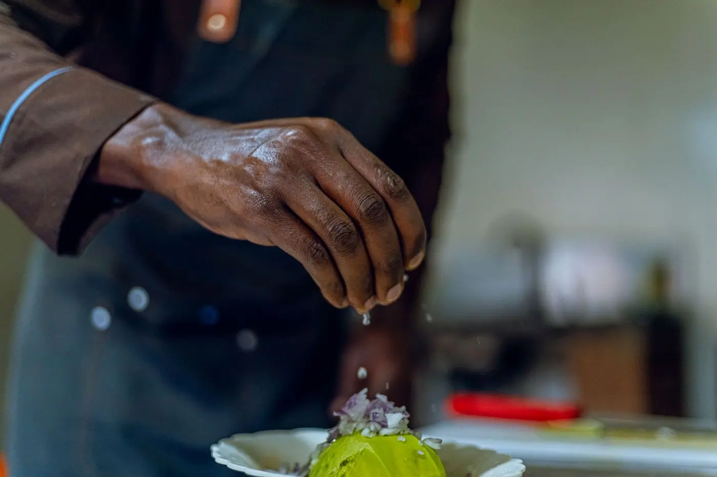 A cook seasoning a dish by hand at the pass