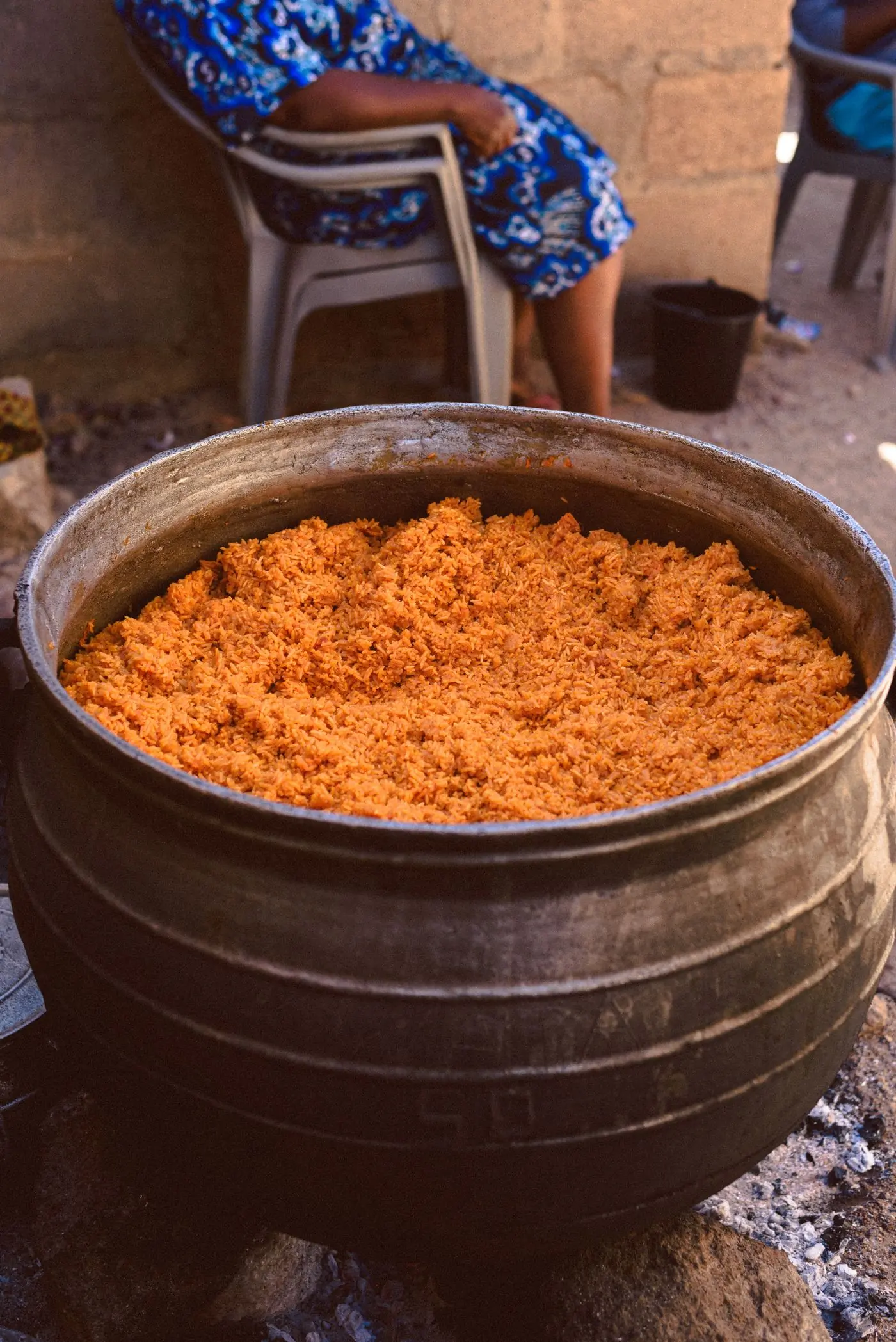 A pot of jollof rice cooking over an open fire in the yard