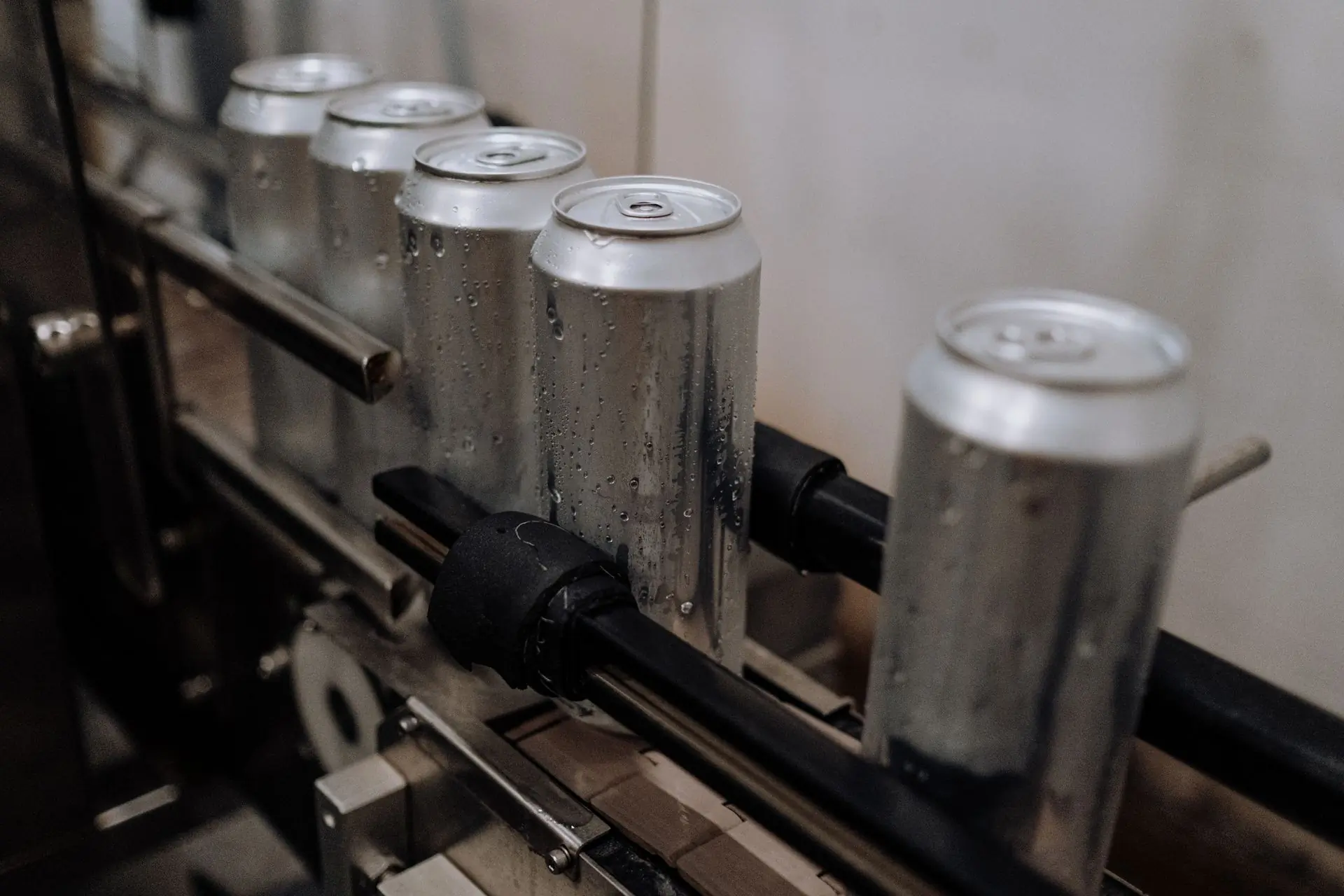Rows of bright soda cans moving down the filling line, a gloved hand steadying the row