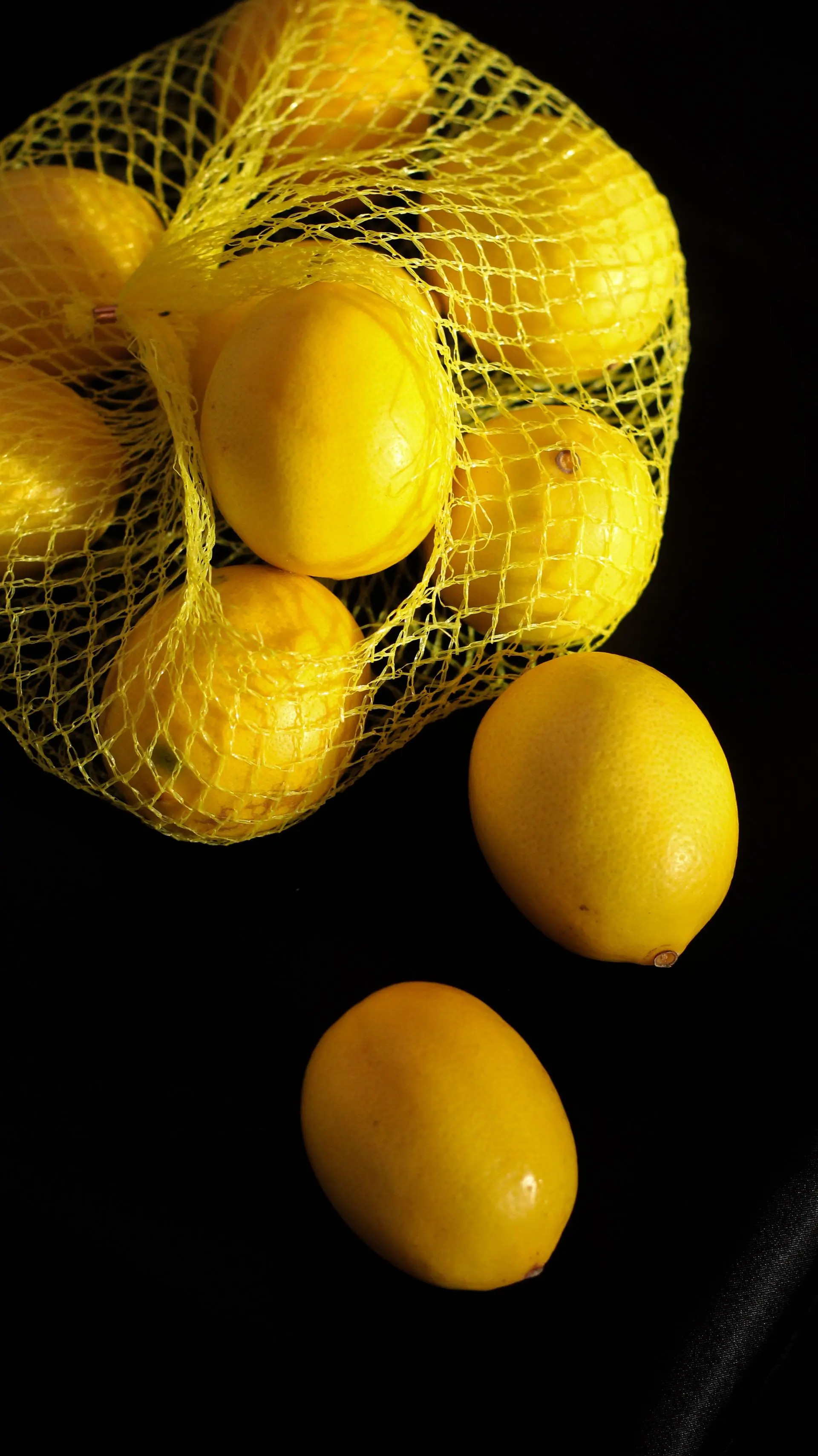 Lemons spilling from a yellow net bag against black