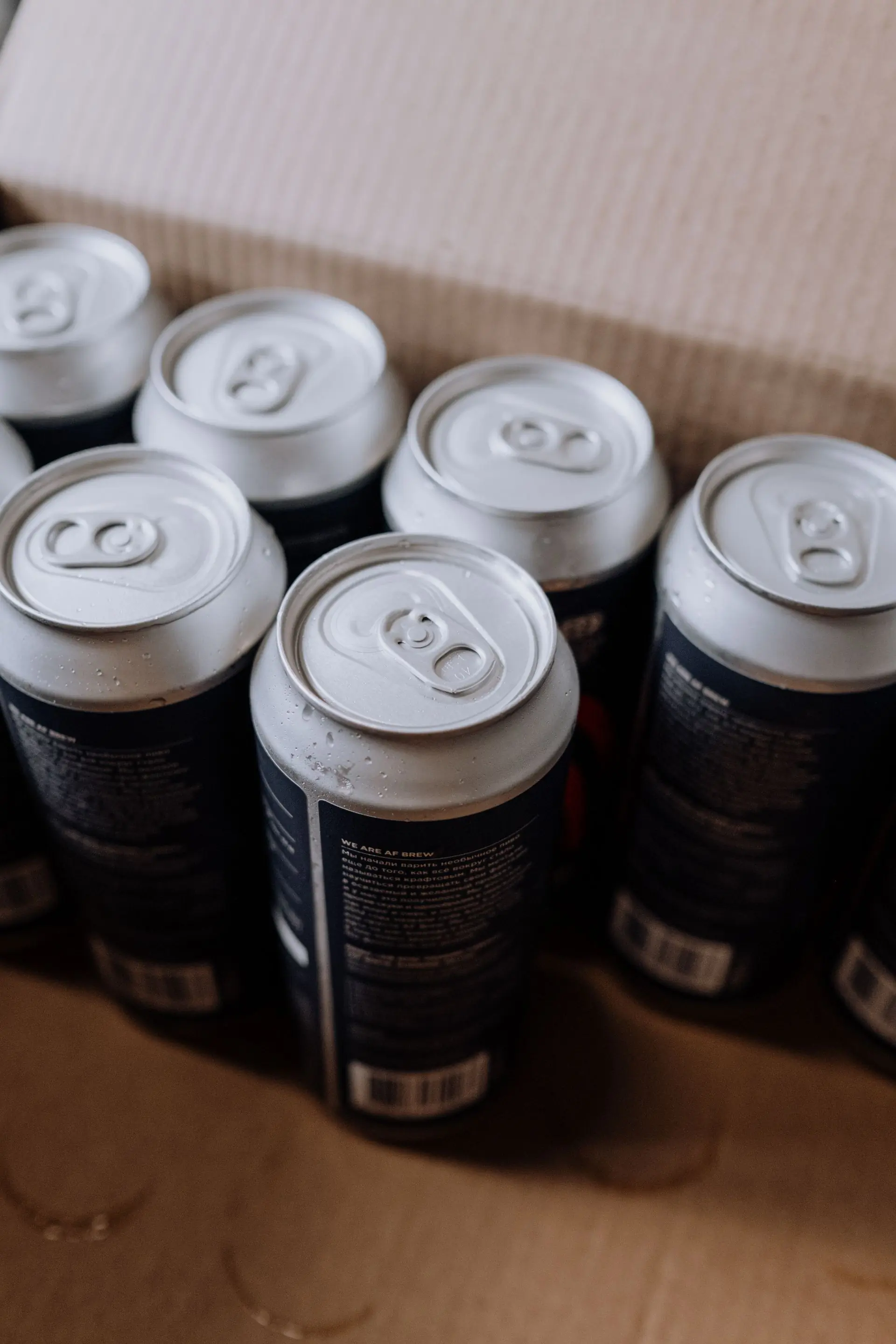Dark cans with condensation packed shoulder to shoulder in a cardboard box