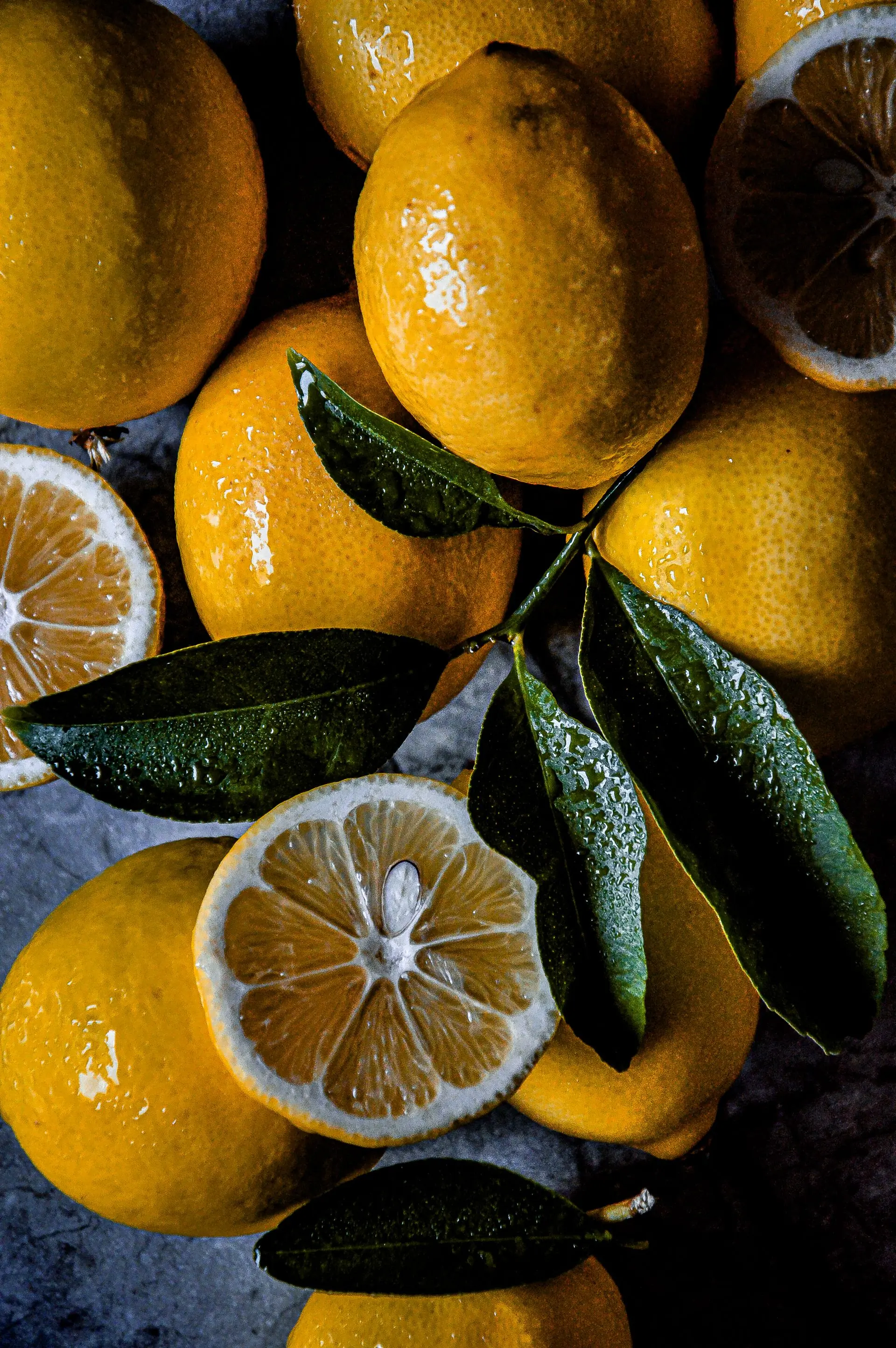 Wet lemons with dark leaves laid on dark marble