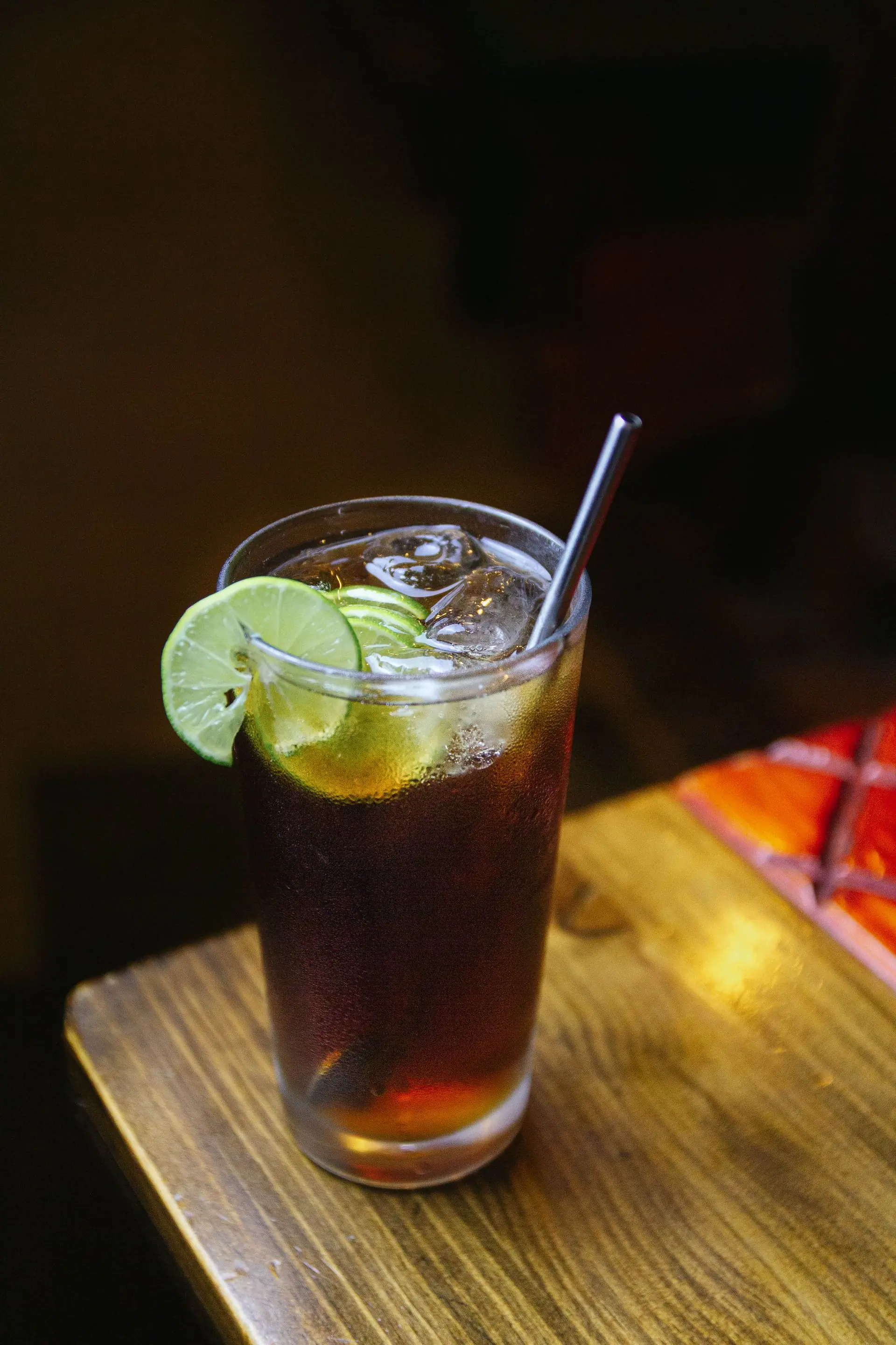 A dark cola drink poured long over ice with lime