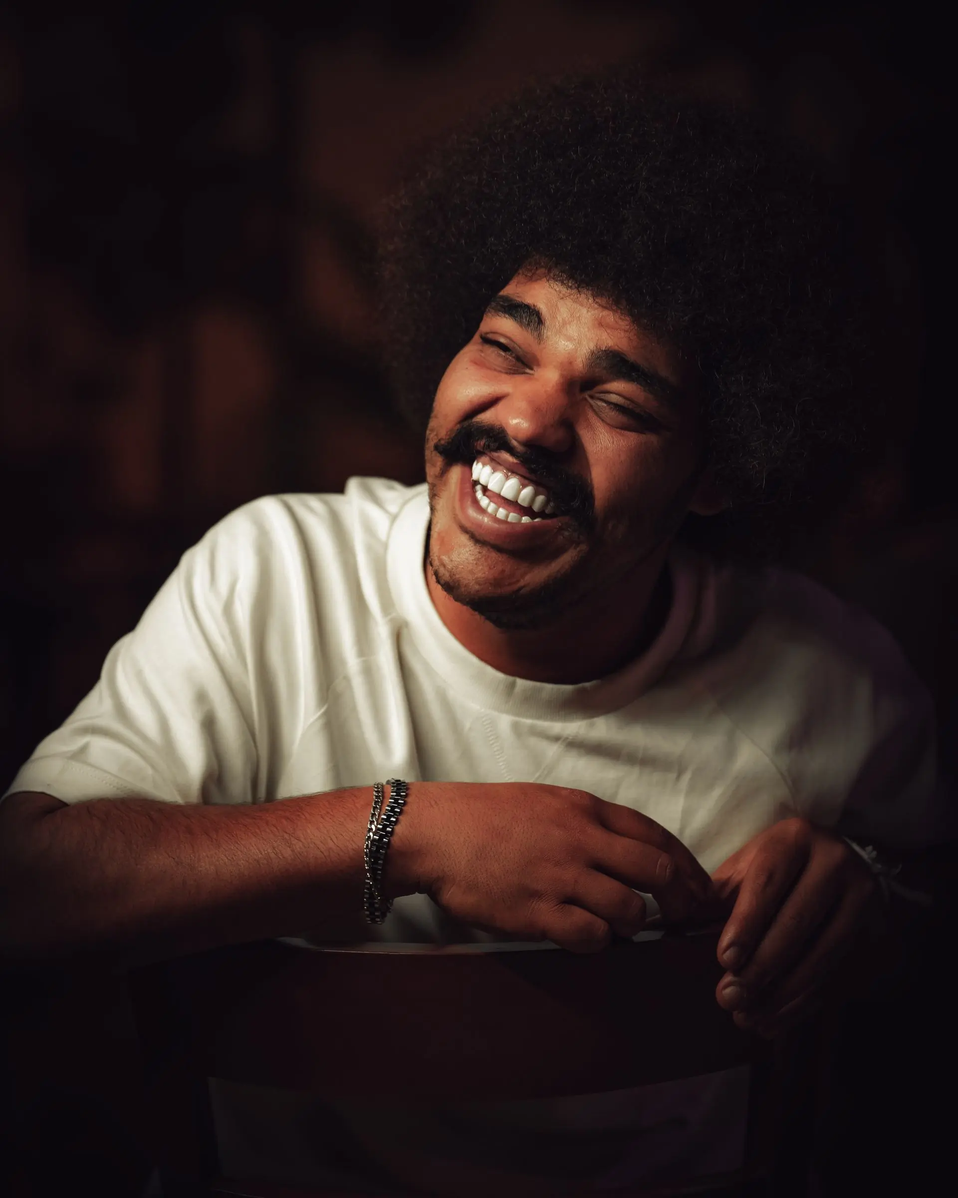 A man with an afro and moustache laughing against warm darkness
