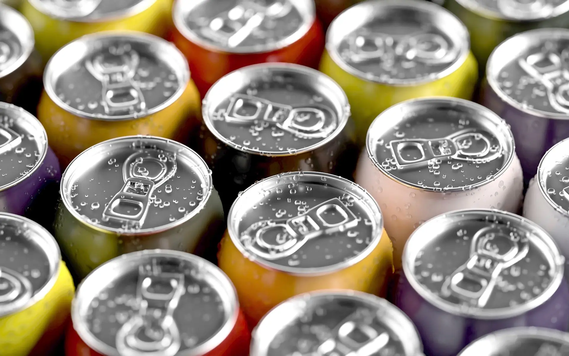 Six differently coloured soda cans packed shoulder to shoulder, tops beaded with cold