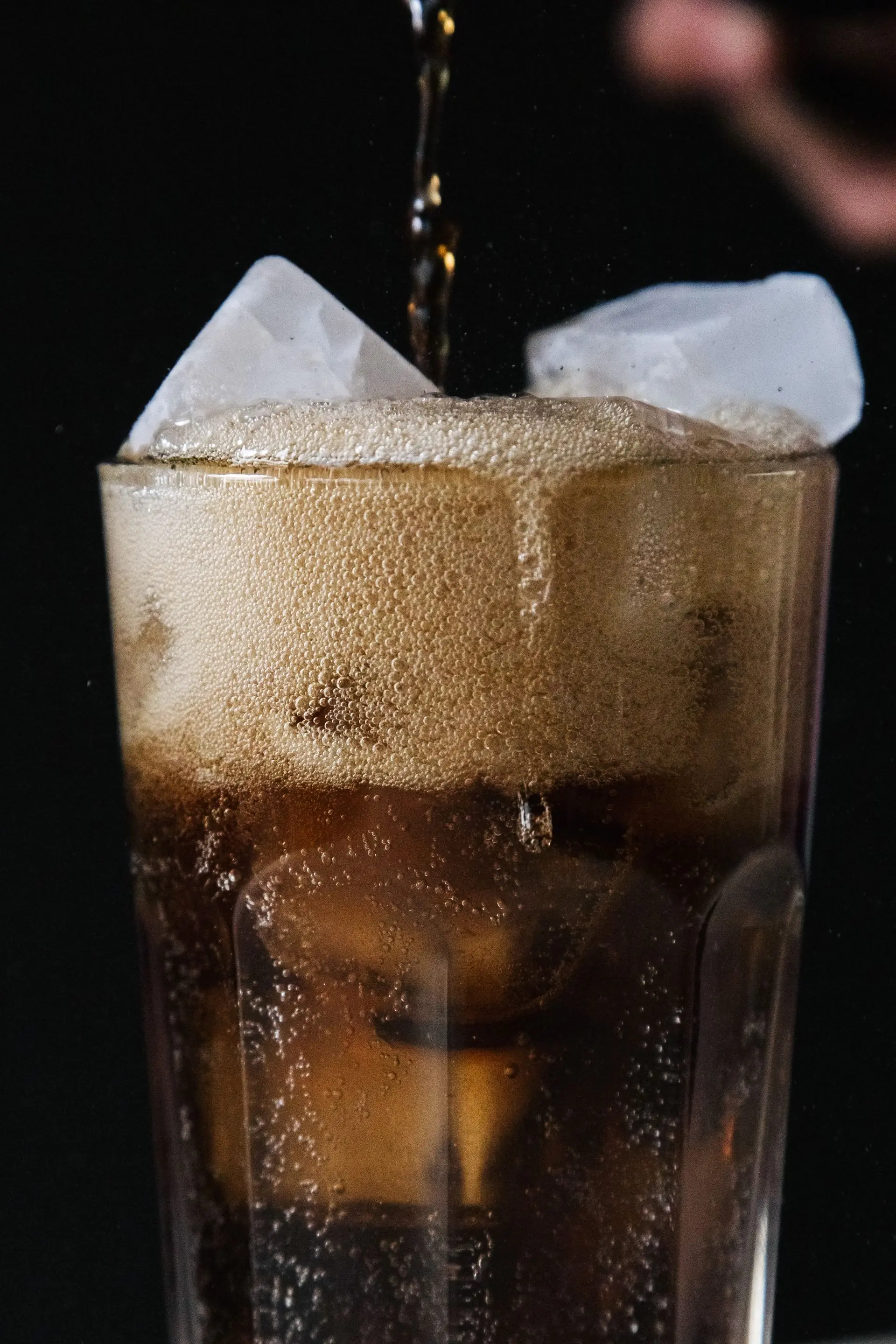 A stream of cola pouring into an iced glass on a dark ground