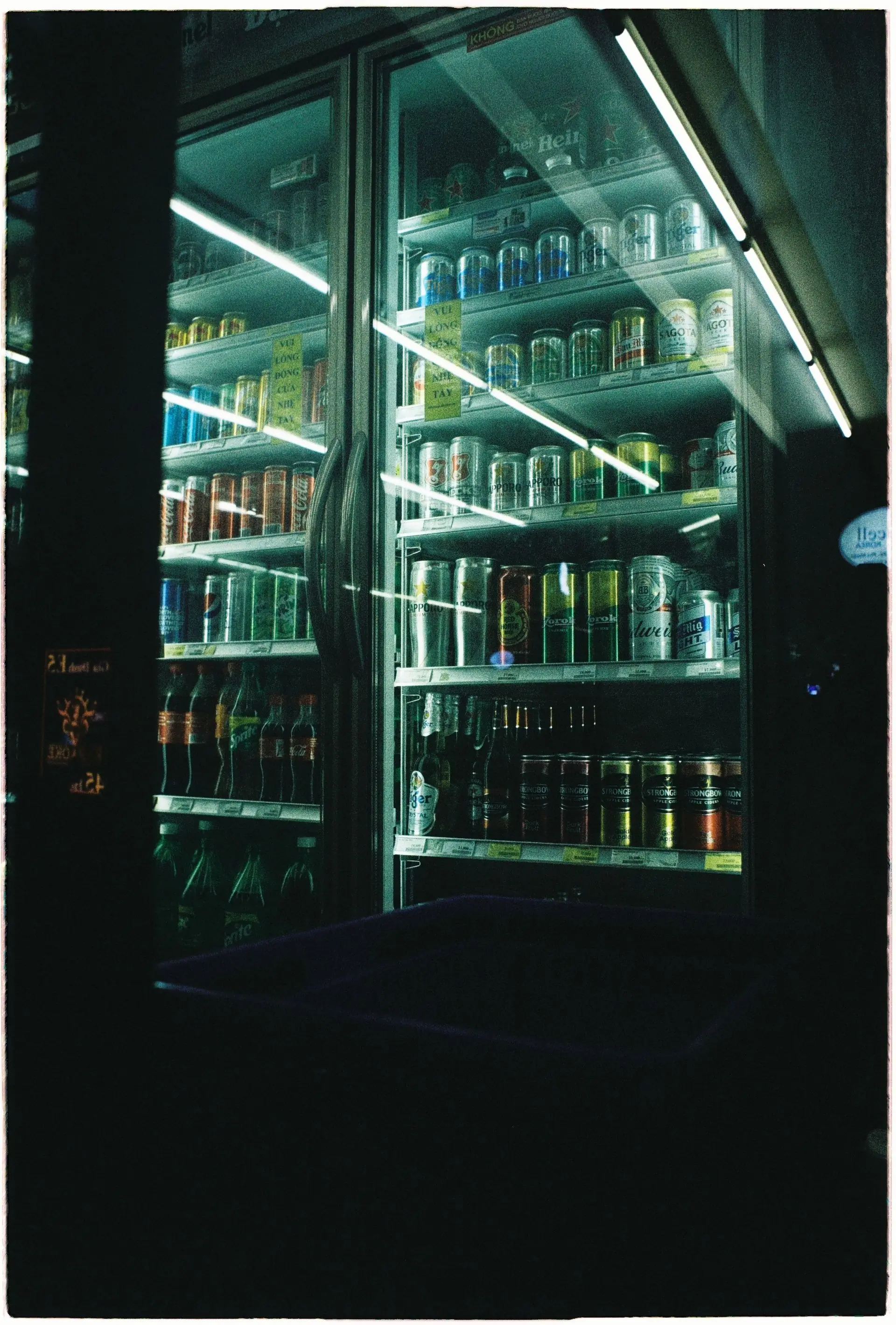 Rows of brightly coloured soda cans chilling on the shelf of a dark fridge