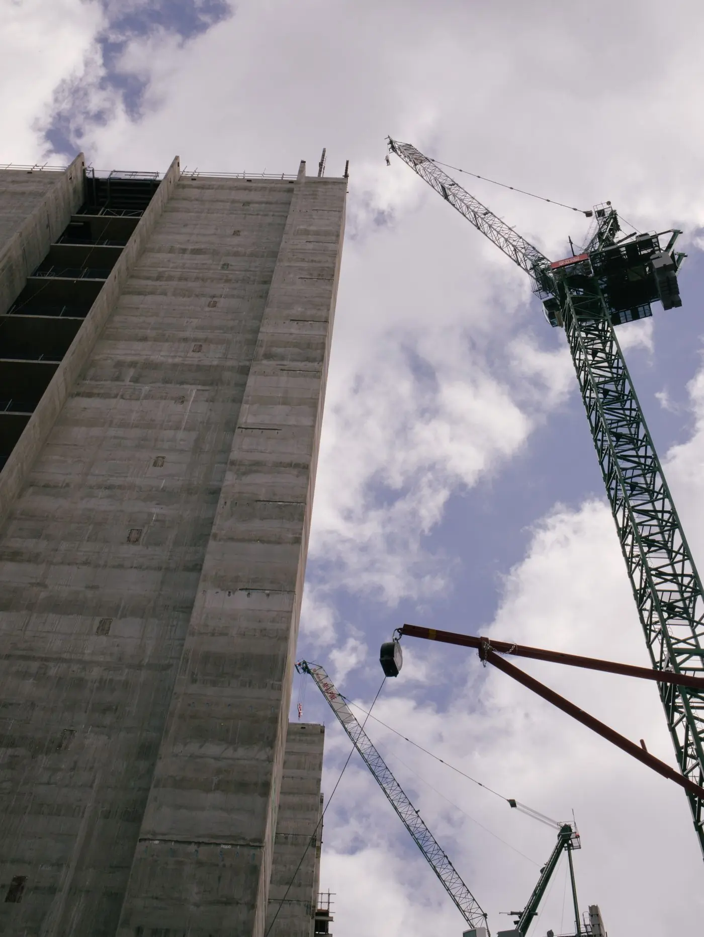 A concrete frame rising beside its tower crane
