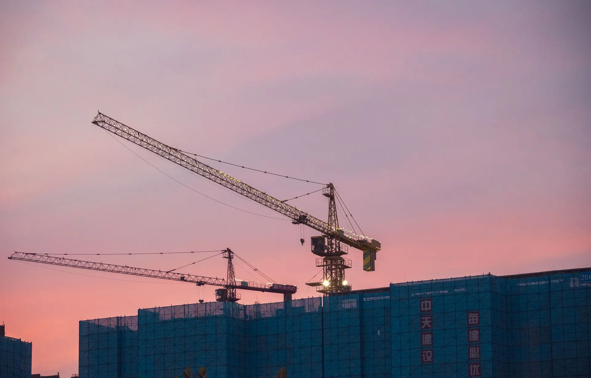 Tower cranes standing over a rising block at dusk
