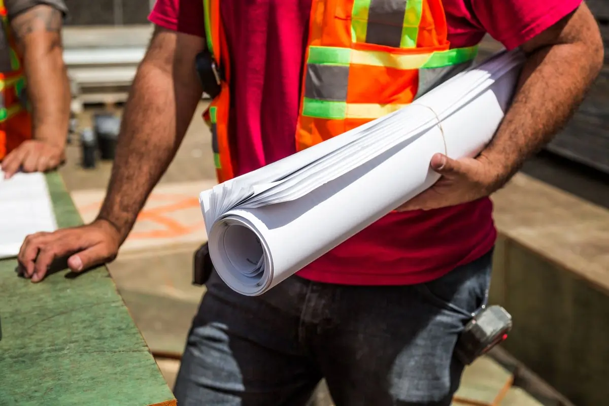 A site engineer carrying a rolled set of drawings