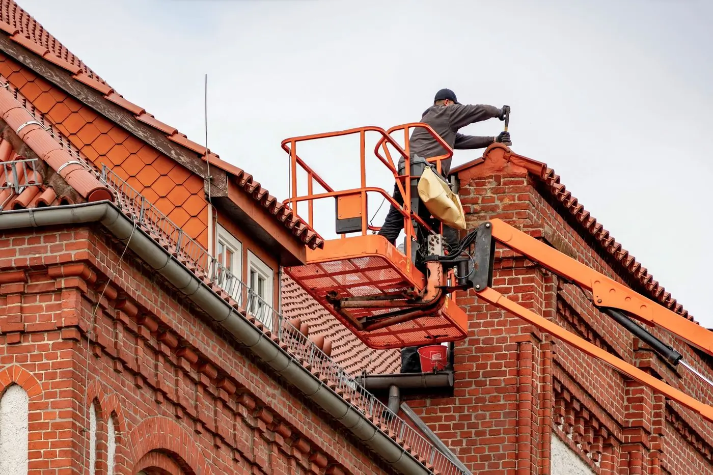 A roofer working from a cherry picker at the ridge of a tiled roof